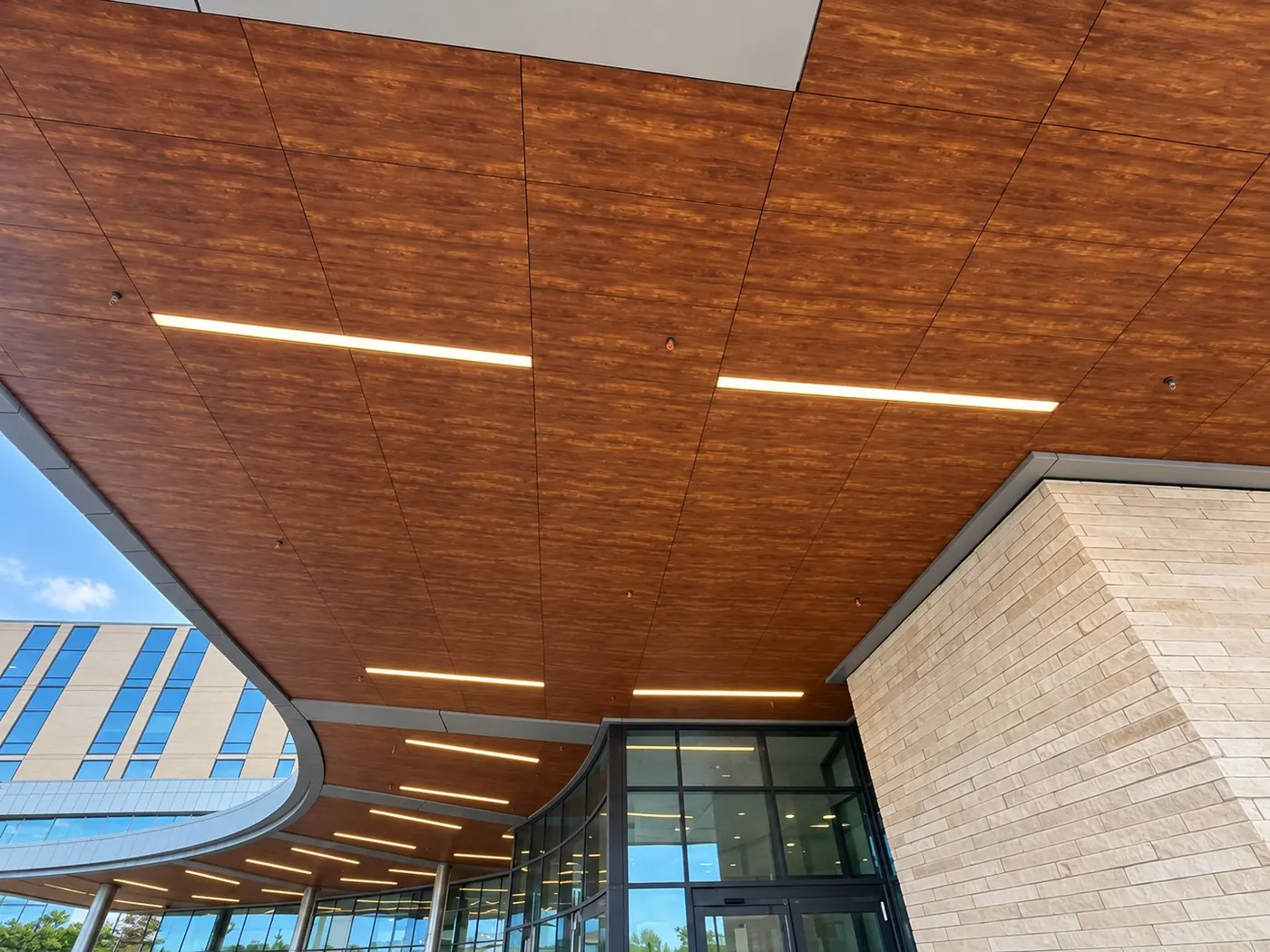 Wood-look specialty ceiling panels with linear lighting at the curved entrance canopy of University Health Retama Hospital